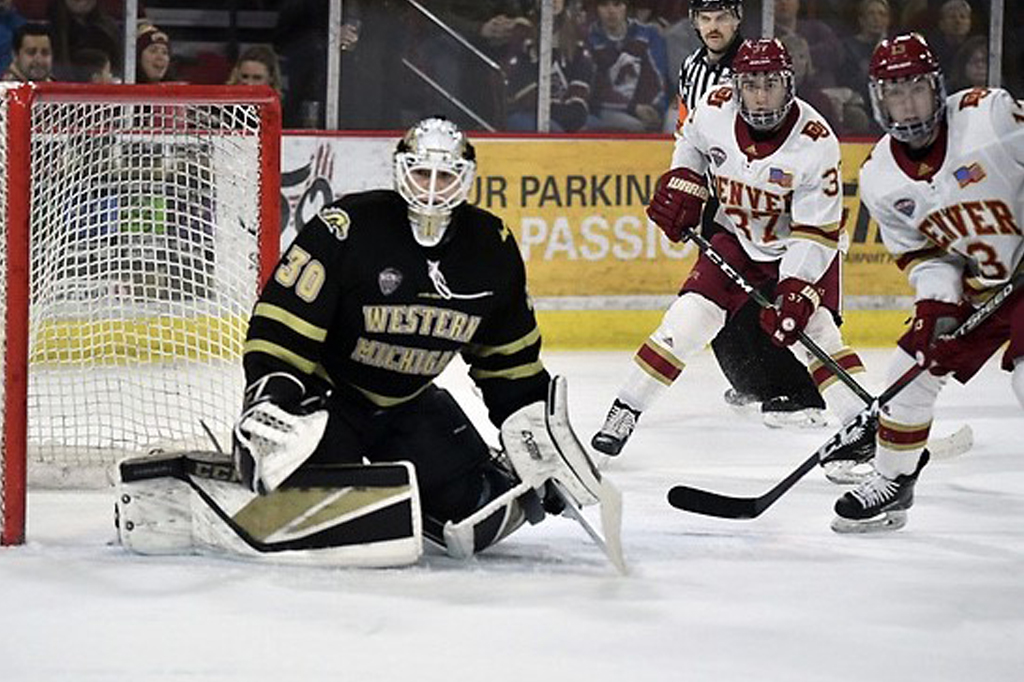 Hockey goalie in black and gold pads defends against an approaching player.