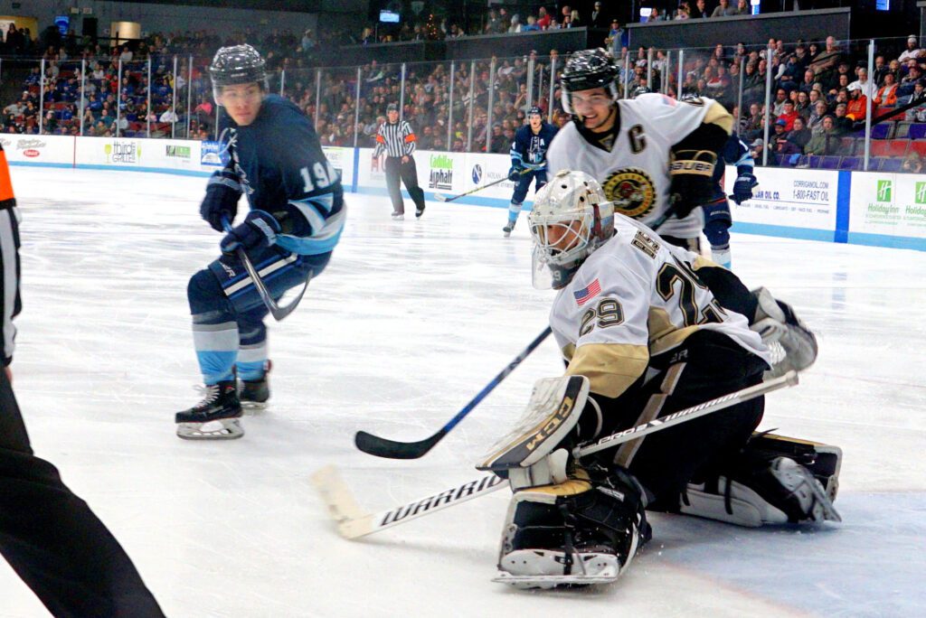 Hockey goalie makes a save while a player watches.